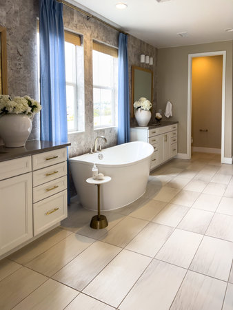 Spacious modern bathroom featuring a white freestanding bathtub, light-colored vanity, and tiled...