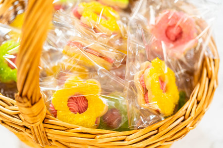 Colorful flower-shaped Easter cookie sandwiches with raspberry buttercream filling, individually wrapped and arranged in a wicker basket. Perfect for spring gifting, Easter parties, and festive dessert tables. Recipe name: Easter Cookie Sandwich with Raspberry Buttercreamの写真素材