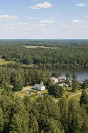 An aerial view shows a peaceful countryside landscape with homes surrounded by dense forest and a small lake. The scene is bathed in daylight, reflecting tranquility and connection with nature.の素材
