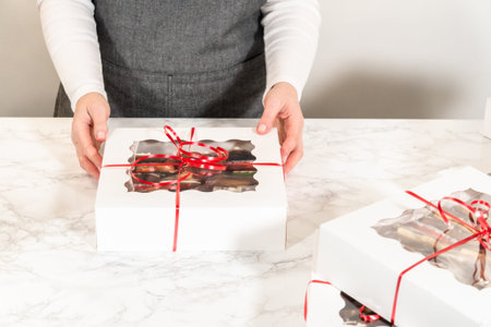 A close-up mid-range shot captures a person carefully preparing a white holiday cookie gift box with...