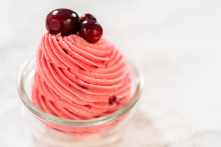 A swirl of vibrant cranberry buttercream piped into a glass jar and topped with fresh cranberries. This creamy, tart frosting is perfect for cookies, cakes, and holiday desserts.の写真素材