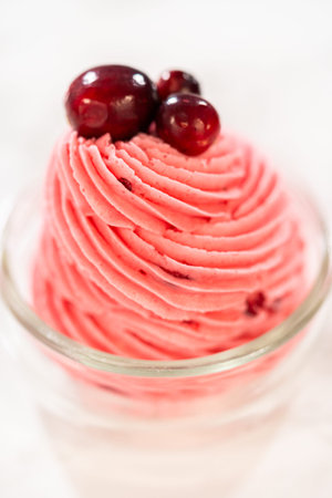A swirl of vibrant cranberry buttercream piped into a glass jar and topped with fresh cranberries. This creamy, tart frosting is perfect for cookies, cakes, and holiday desserts.の写真素材
