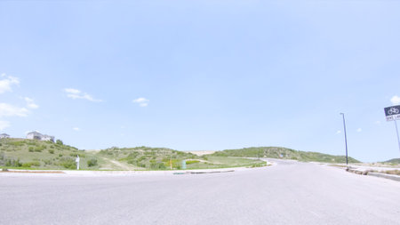 A clean curved road in Castle Rock, Colorado runs beside a grassy hill under a clear sky. A street...