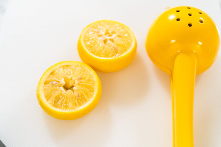 Two halves of a freshly squeezed lemon rest on a white surface beside a vibrant yellow citrus...