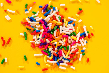 Macro shot of multicolored candy sprinkles scattered on a vibrant yellow surface. Perfect for...