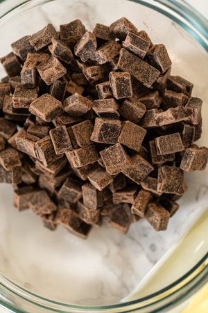 A macro view of dark chocolate chunks piled in a glass bowl on marble background. This close-up...