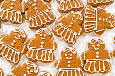A large batch of gingerbread girl cookies featuring uniform royal icing designs, arranged to showcase the intricate dress and hair details.の写真素材
