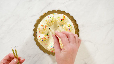 Close-up of a hand placing metallic gold birthday candles on a sprinkle cake topped with buttercream...