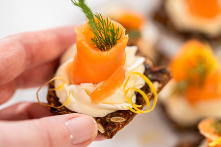 A gourmet smoked salmon canape elegantly arranged on a crispy cracker, topped with a swirl of smooth cream cheese, fresh thyme, and a drizzle of olive oil. The vibrant orange salmon contrasts beautifully with the rich, creamy base, creating a visually stunning and flavorful appetizer. Perfect for holiday gatherings, cocktail parties, or fine dining presentations.の写真素材