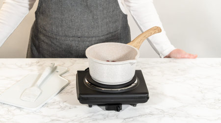 A small saucepan on a stovetop containing cranberries, being heated to create a fresh cranberry...