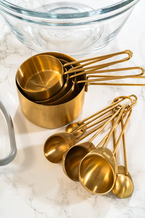 A flat lay view of gold measuring cups and spoons elegantly arranged on a marble surface. These...