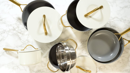 A ceramic cookware set with steamer insert and gold-handled lids is spread across a marble...