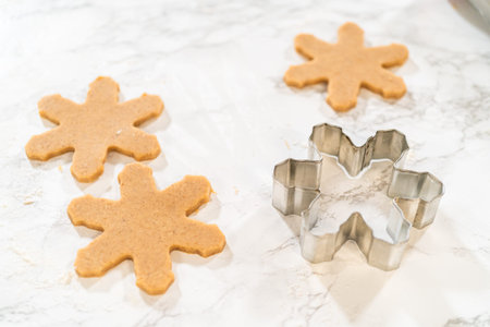 Overhead view showing a snowflake-shaped cookie cutter placed between freshly cut amber gingerbread...