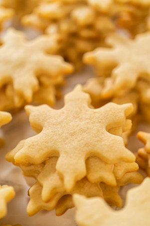 Golden, freshly baked cut-out sugar cookies shaped like festive snowflakes, cooling on a flat...