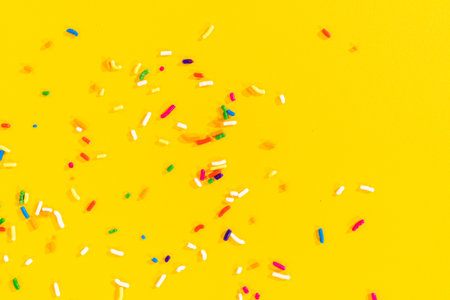 An assortment of colorful rainbow sprinkles scattered across a bright yellow surface. Perfect for use in baking-themed designs, dessert backgrounds, or party invitations.の写真素材