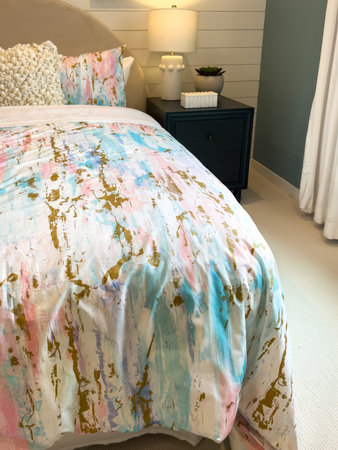 A cozy bedroom features a bed with a colorful patterned bedspread. The space includes a nightstand,...