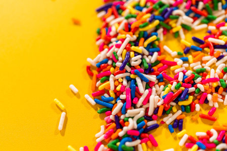 A macro view of rainbow sprinkles arranged in the upper right corner of a yellow surface. The...