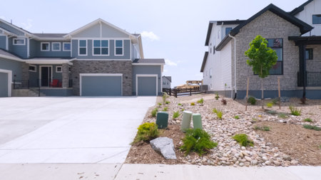 A modern two-story home with a wide concrete driveway and decorative xeriscaped yard including rock beds and young plants. The property sits under clear skies.
