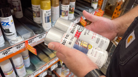 Parker, Colorado, USA-September 22, 2024 - A close-up of a man in a dark shirt holding two Rust-Oleum spray paint cans in a home improvement store. The background shows a shelf filled with similar paint products and visible price labels. The lighting is s