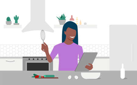 A young black woman looks on tablet and cooking by online video tutorial in her kitchen. Online culinary school. Online courses, e-learning.のイラスト素材