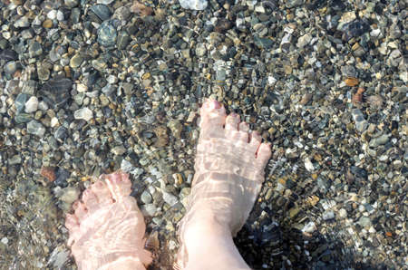 women's feet on the beach in sea waterの写真素材