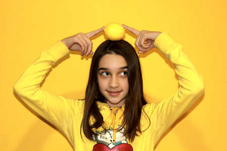 a girl plays with a lemon on a yellow backgroundの写真素材