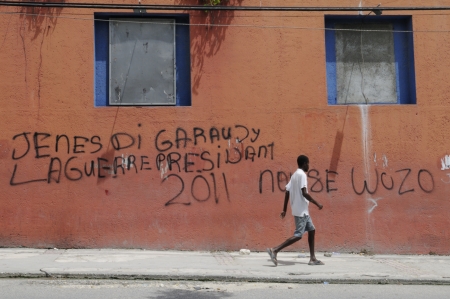 PORT-AU-PRINCE - AUGUST 21: A young man passing by a graffiti on the wall which supports the candidature of Wycleaf Jean as the President, in Port-Au-Prince, Haiti on August 21, 2010.のeditorial素材