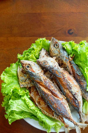 Fried mackerel and lettuce in dish on wooden table, Thai food style.の写真素材