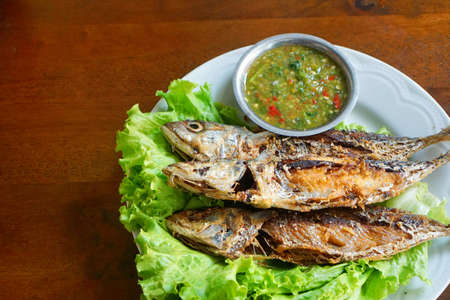 Fried mackerel and lettuce in dish on wooden table, Thai food style.の写真素材