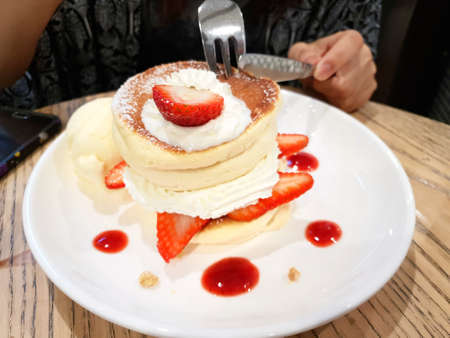 Women eating strawberry pancakes with icing ,whipping cream and ice cream vanilla on wooden...