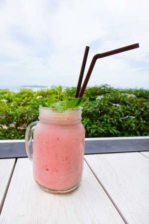 Strawberry smoothie or milkshake in jar with Mint leaves on wooden table. on tree and blue sky background. Summer drink, healthy food. space for your text. Top viewの写真素材