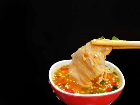 Closeup of sliced pork hold with chopsticks dipping in spicy sauce at restaurant, Shabu is korea traditional or Sukiyaki is japanese traditional, Space for text in templateの写真素材
