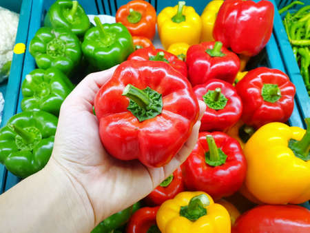 Top view of hand holding fresh red bell peppers for sale in the supermarket at Thailand on blurred...