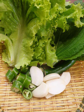 Selective focus of lettuce, hoary basil,green pepper with slices and garlic cut into slices on wooden basket (Asteraceae,Capsicum annuum, bell pepper, sweet pepper,Allium sativum, Lactuca sativa)の写真素材