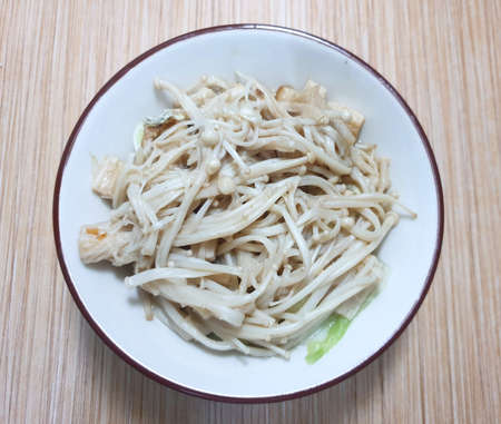 Top view of Stir fried Golden Mushroom or Enokitake with butter on white plate, on wooden table...