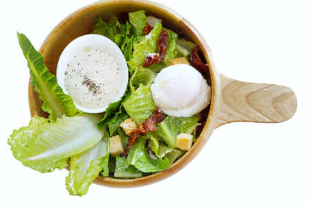 Top view of mixed vegetable salad with fresh lettuce, green oak, bread, boiled egg, fried bacon and salad dressing in wooden bowl isolated on white background, caesar salad, healthy food conceptの写真素材