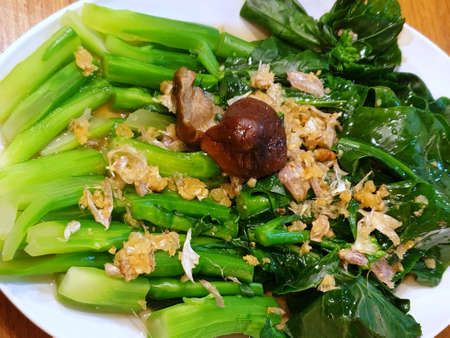 Top view of stir fried chinese kale topping with fried garlic in white plate as a background in...