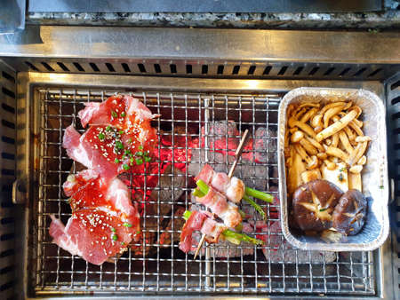 Top view of grilled pork sliced and bacon wrapped asparagus on skewer with garlic and mushroom on the charcoal stove in Japanese restaurant (Bacon Asparagus)の写真素材
