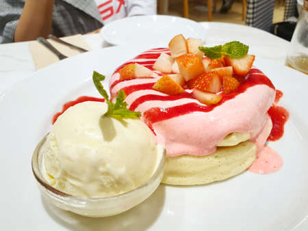 Top view of pancake dessert topping with strawberry sauce and strawberry slice and ice cream vanilla in white plate on blurred woman as a background in cafÃ©, ready to eat or serveの写真素材
