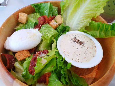 Blurred image of mixed vegetable salad with fresh lettuce, green oak, bread, boiled egg, fried bacon and salad dressing in wooden bowl as a background, caesar salad, healthy food conceptの写真素材