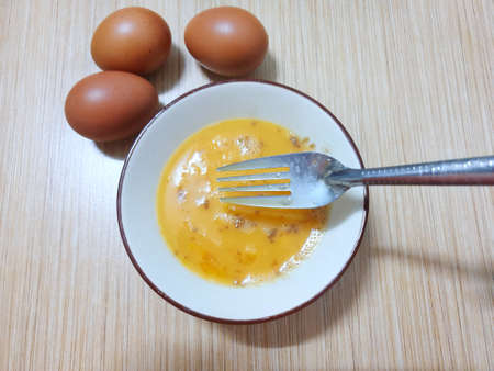 Top view of beat the egg yolks into a bubble with pepper and soy sauce waiting to cook, on wooden...