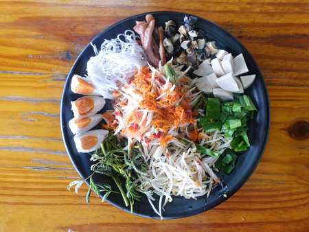 Thai food style, Top view of papaya salad set in black plate on wooden table, Space for text in template, healthy food concept, Som Tum tad is Thai traditionalの写真素材
