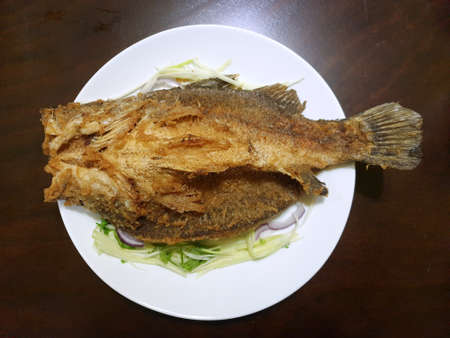 Thai food style, Fried snapper on mango sliced in white ceramic plate on wooden table, top view,This...
