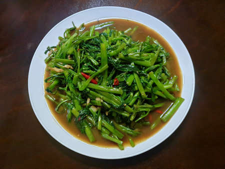 Top view of fried water spinach seasoned with chili and soy sauce on wooden table as a background,...