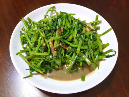 Top view of fried water spinach seasoned with chili and soy sauce on white plate on wooden table in restaurantの写真素材