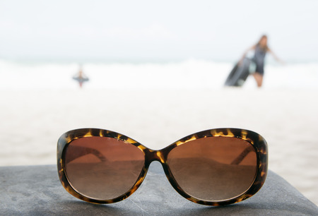 Sunglasses putting on rock table with people playing on the beach.の写真素材