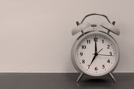 Black and white of seven o'clock modern alarm clock on wooden table.
