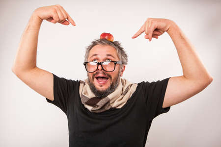 Crazy looking old man with grey beard nerd big glasses funny showing on apple on head with both handsの写真素材