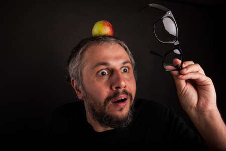 Old man with beard and big nerd glasses with apple on head is surprisedの写真素材