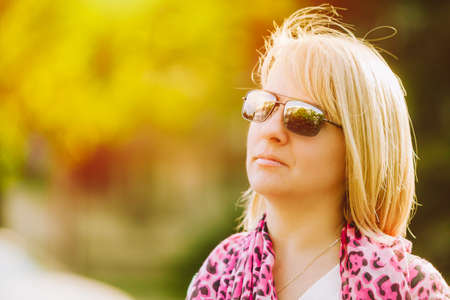 Young beautiful confident blond woman in sunglasses and pink leopard scarf walking in windy summer...